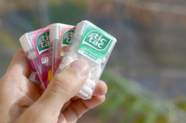 Hand holds three Tic Tac Candy packages of different tastes close up. Tic tac is popular due its minty fresh taste and easy to carry. Hard mints produced by Ferrero since 1968 clipart