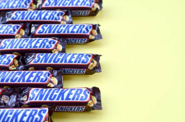 Birçok Snickers çikolatası pastel sarı kağıdın üzerinde yatar. Snickers çikolataları Mars Anonim Şirketi tarafından üretilir. Snickers 1930 yılında Franklin Clarence Mars tarafından yaratıldı.