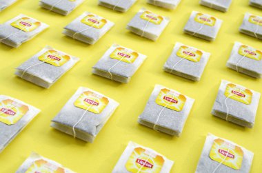 Pastel sarı yüzeyde Lipton Sarı Etiketli siyah çay poşetleri vardı. Lipton dünyaca ünlü bir çay türüdür.