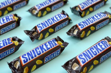 Many Snickers chocolate bars lies on pastel blue paper. Snickers bars are produced by Mars Incorporated. Snickers was created by Franklin Clarence Mars in 1930