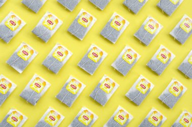 Pastel sarı yüzeyde Lipton Sarı Etiketli siyah çay poşetleri vardı. Lipton dünyaca ünlü bir çay türüdür.