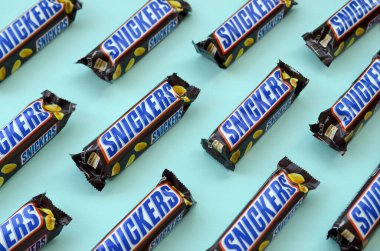 Many Snickers chocolate bars lies on pastel blue paper. Snickers bars are produced by Mars Incorporated. Snickers was created by Franklin Clarence Mars in 1930