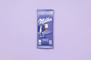 Eflatun arkaplana sarılmış klasik menekşe rengi Milka çikolatası tableti. Milka, 1901 'de İsviçre' de üretilen bir çikolata markasıdır.