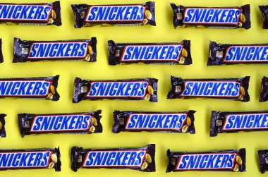 Birçok Snickers çikolatası pastel sarı kağıdın üzerinde yatar. Snickers çikolataları Mars Anonim Şirketi tarafından üretilir. Snickers 1930 yılında Franklin Clarence Mars tarafından yaratıldı.