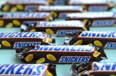Many Snickers chocolate bars lies on pastel blue paper. Snickers bars are produced by Mars Incorporated. Snickers was created by Franklin Clarence Mars in 1930