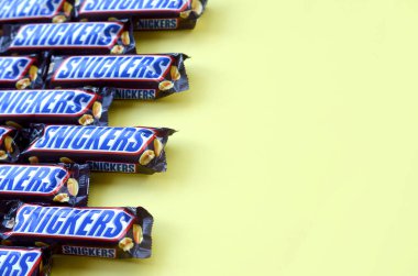 Birçok Snickers çikolatası pastel sarı kağıdın üzerinde yatar. Snickers çikolataları Mars Anonim Şirketi tarafından üretilir. Snickers 1930 yılında Franklin Clarence Mars tarafından yaratıldı.