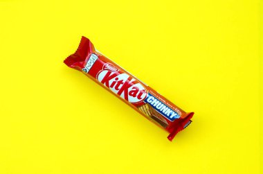 Kit Kat chocolate bar in red wrapping lies on bright yellow background. Kit kat created by Rowntree's of York in United Kingdom and is now produced globally by Nestle