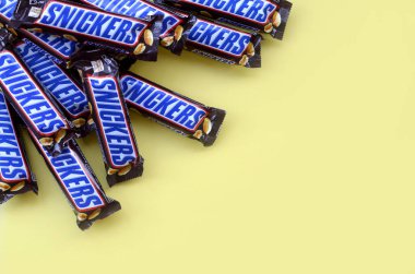 Birçok Snickers çikolatası pastel sarı kağıdın üzerinde yatar. Snickers çikolataları Mars Anonim Şirketi tarafından üretilir. Snickers 1930 yılında Franklin Clarence Mars tarafından yaratıldı.