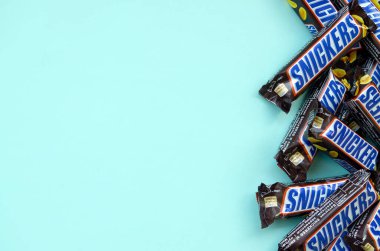 Many Snickers chocolate bars lies on pastel blue paper. Snickers bars are produced by Mars Incorporated. Snickers was created by Franklin Clarence Mars in 1930