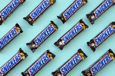 Many Snickers chocolate bars lies on pastel blue paper. Snickers bars are produced by Mars Incorporated. Snickers was created by Franklin Clarence Mars in 1930