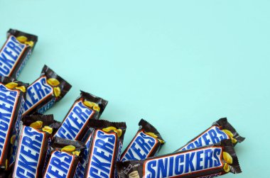 Many Snickers chocolate bars lies on pastel blue paper. Snickers bars are produced by Mars Incorporated. Snickers was created by Franklin Clarence Mars in 1930