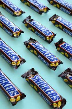 Many Snickers chocolate bars lies on pastel blue paper. Snickers bars are produced by Mars Incorporated. Snickers was created by Franklin Clarence Mars in 1930