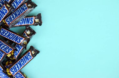 Many Snickers chocolate bars lies on pastel blue paper. Snickers bars are produced by Mars Incorporated. Snickers was created by Franklin Clarence Mars in 1930