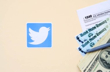 Twitter baskılı logoda 1040 Bireysel Gelir Vergi iade formu ve bej arka planda 100 Dolarlık banknotlar yer alıyor. Sosyal ağ kavramından vergi dönemine yardım