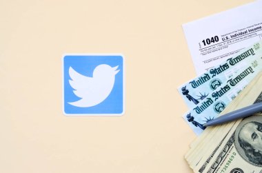 Twitter printed logo lies with 1040 Individual Income tax return form with Refund Check and hundred dollar bills on beige background. Help in tax period from social network concept clipart