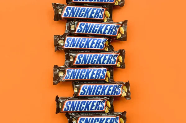 Muchas barras de chocolate Snickers se encuentra en papel naranja pastel. Las barras Snickers son producidas por Mars Incorporated. Snickers fue creado por Franklin Clarence Mars en 1930 — Foto de Stock