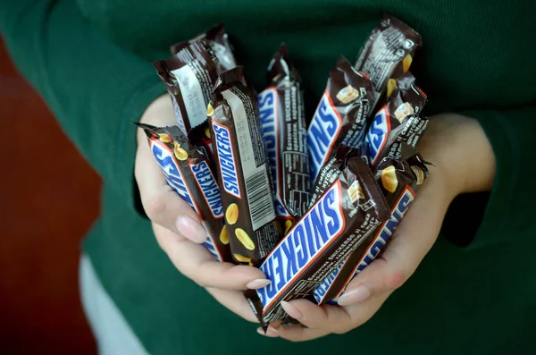 KHARKOV, UCRANIA - 8 DE OCTUBRE DE 2019: Una joven morena caucásica muestra muchas barras de chocolate Snickers en la habitación oscura. Snickers chocolate fabricado por Mars — Foto de Stock