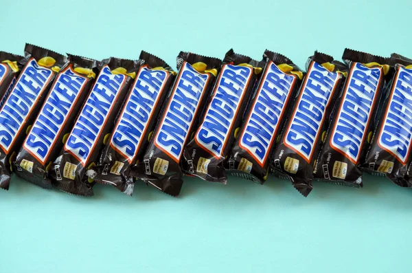 Muitas barras de chocolate Snickers encontra-se no papel azul pastel. Barras Snickers são produzidas pela Mars Incorporated. Snickers foi criado por Franklin Clarence Mars em 1930 — Fotografia de Stock