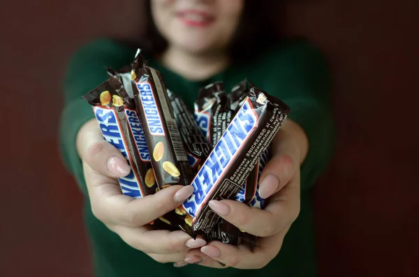 KHARKOV, UCRANIA - 8 DE OCTUBRE DE 2019: Una joven morena caucásica muestra muchas barras de chocolate Snickers en la habitación oscura. Snickers chocolate fabricado por Mars — Foto de Stock