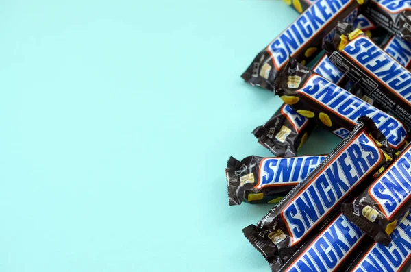 Muitas barras de chocolate Snickers encontra-se no papel azul pastel. Barras Snickers são produzidas pela Mars Incorporated. Snickers foi criado por Franklin Clarence Mars em 1930 — Fotografia de Stock