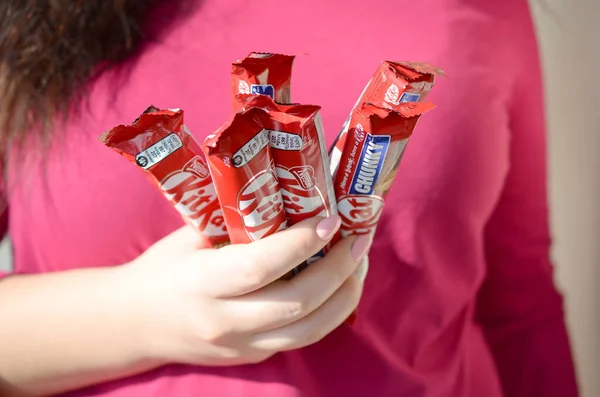 KHARKOV, UCRANIA - 21 DE OCTUBRE DE 2019: Una joven morena caucásica sostiene muchas barras de chocolate kat kit en envoltura roja en la habitación de luz. Kit Kat chocolate fabricado por Nestlé —  Fotos de Stock