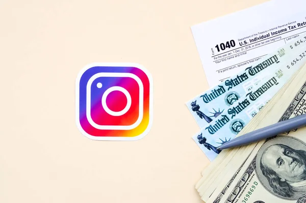 Instagram gedrucktes Logo mit 1040 individuellen Einkommensteuererklärungen mit Rückerstattungsscheck und Hundert-Dollar-Scheinen auf beigem Hintergrund. Hilfe in Steuerzeit aus sozialem Netzwerk-Konzept — Stockfoto