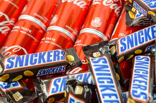 Snickers barras de chocolate en envoltura marrón se encuentra en latas de lata de Coca Cola rojo de cerca. Famoso producto de bebida y chocolate —  Fotos de Stock