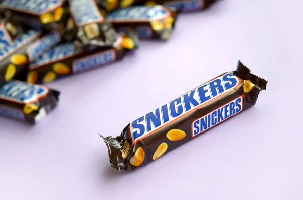 Många Snickers chokladkakor ligger på pastellpapper. Snickers barer tillverkas av Mars Incorporated. Snickers skapades av Franklin Clarence Mars 1930 — Stockfoto