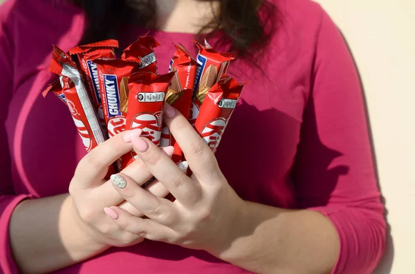 KHARKOV, UCRANIA - 21 DE OCTUBRE DE 2019: Una joven morena caucásica sostiene muchas barras de chocolate kat kit en envoltura roja en la habitación de luz. Kit Kat chocolate fabricado por Nestlé —  Fotos de Stock