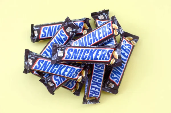 Muchas barras de chocolate Snickers se encuentra en papel amarillo pastel. Las barras Snickers son producidas por Mars Incorporated. Snickers fue creado por Franklin Clarence Mars en 1930 — Foto de Stock