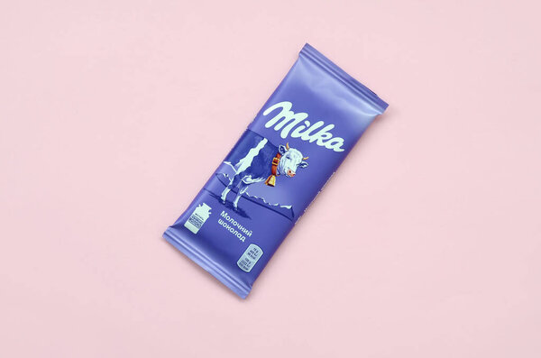Milka chocolate tablet in classic violet wrapping on pastel pink background. Milka is brand of chocolate confection originated in Switzerland in 1901