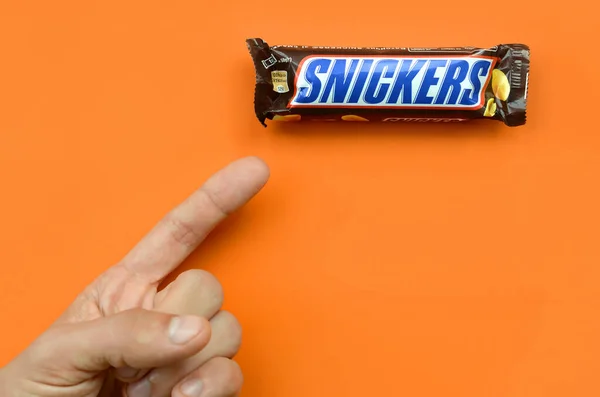 Mão segurando uma barra de chocolate Snickers. Barras Snickers são produzidas pela Mars Incorporated. Snickers foi criado por Franklin Clarence Mars em 1930 — Fotografia de Stock