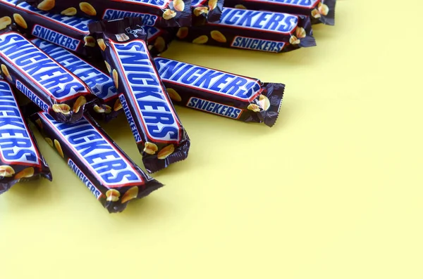 Mnoho čokoládových tyčinek Snickers leží na pastelově žlutém papíru. Tyčinky Snickers vyrábí společnost Mars Incorporated. Snickers vytvořil Franklin Clarence Mars v roce 1930 — Stock fotografie