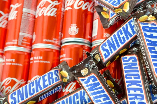 Barras de chocolate Snickers em marrom embrulho mentiras em latas de lata de Coca-Cola vermelho de perto. Bebida famosa e produto de chocolate — Fotografia de Stock