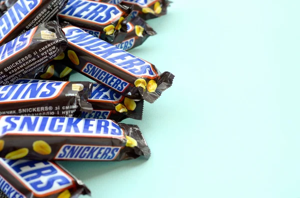 Muchas barras de chocolate Snickers se encuentra en papel azul pastel. Las barras Snickers son producidas por Mars Incorporated. Snickers fue creado por Franklin Clarence Mars en 1930 —  Fotos de Stock