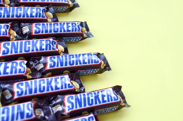 Veel Snickers chocoladerepen liggen op pastelgeel papier. Snickers bars worden geproduceerd door Mars Incorporated. Snickers is gemaakt door Franklin Clarence Mars in 1930. — Stockfoto