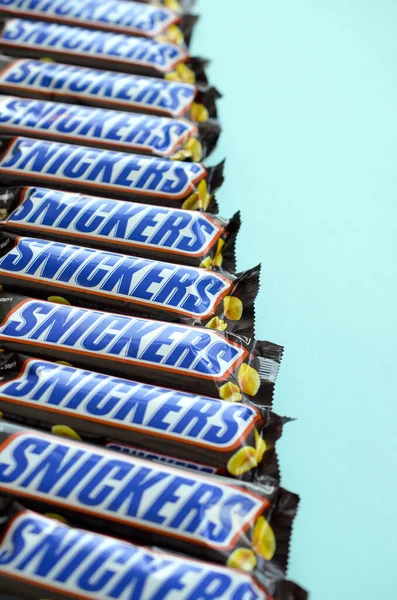 Muitas barras de chocolate Snickers encontra-se no papel azul pastel. Barras Snickers são produzidas pela Mars Incorporated. Snickers foi criado por Franklin Clarence Mars em 1930 — Fotografia de Stock