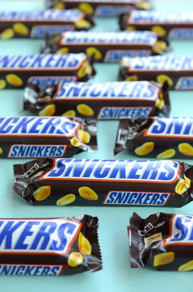 Muchas barras de chocolate Snickers se encuentra en papel azul pastel. Las barras Snickers son producidas por Mars Incorporated. Snickers fue creado por Franklin Clarence Mars en 1930 — Foto de Stock