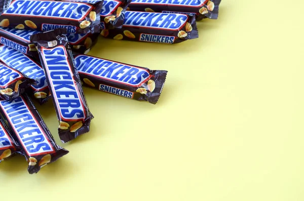 Veel Snickers chocoladerepen liggen op pastelgeel papier. Snickers bars worden geproduceerd door Mars Incorporated. Snickers is gemaakt door Franklin Clarence Mars in 1930. — Stockfoto