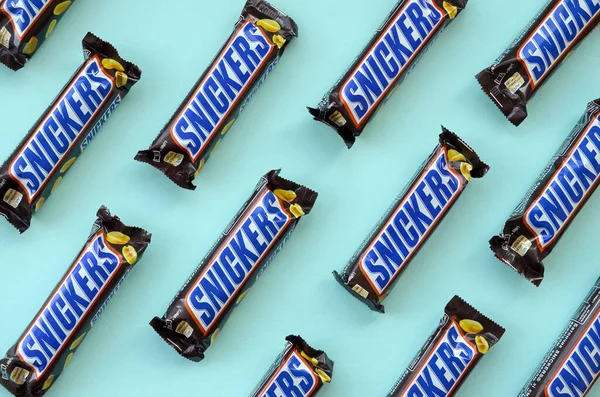 Muchas barras de chocolate Snickers se encuentra en papel azul pastel. Las barras Snickers son producidas por Mars Incorporated. Snickers fue creado por Franklin Clarence Mars en 1930 — Foto de Stock