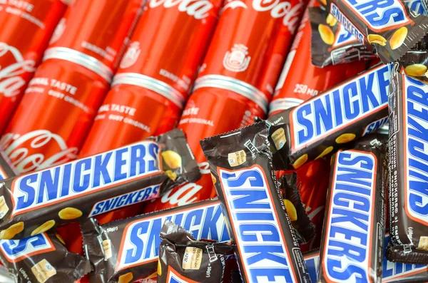 Snickers barras de chocolate en envoltura marrón se encuentra en latas de lata de Coca Cola rojo de cerca. Famoso producto de bebida y chocolate —  Fotos de Stock