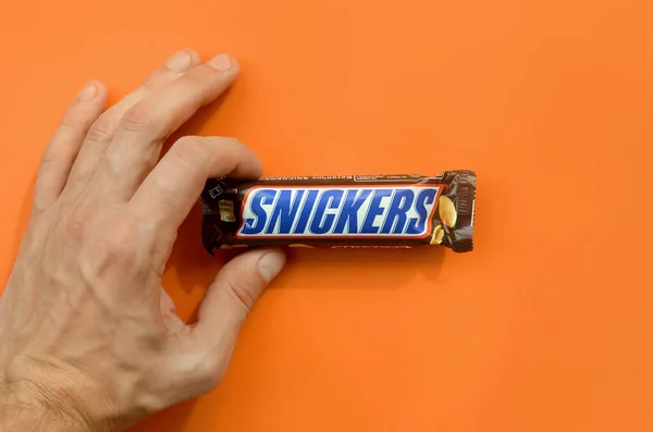 Hånd som holder en Snickers sjokolade. Snickers-barer produseres av Mars Incorporated. Snickers ble skapt av Franklin Clarence Mars i 1930. – stockfoto