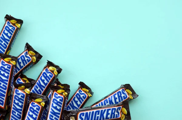 Muchas barras de chocolate Snickers se encuentra en papel azul pastel. Las barras Snickers son producidas por Mars Incorporated. Snickers fue creado por Franklin Clarence Mars en 1930 —  Fotos de Stock