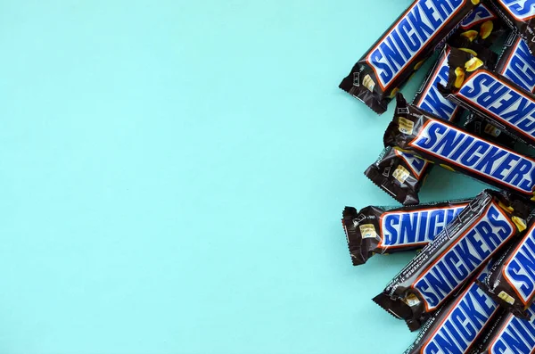 Muitas barras de chocolate Snickers encontra-se no papel azul pastel. Barras Snickers são produzidas pela Mars Incorporated. Snickers foi criado por Franklin Clarence Mars em 1930 — Fotografia de Stock