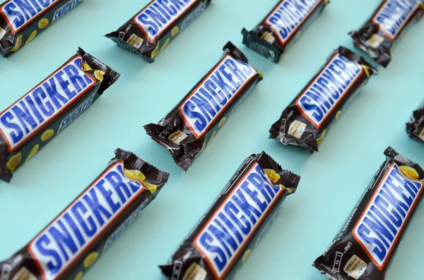 Muchas barras de chocolate Snickers se encuentra en papel azul pastel. Las barras Snickers son producidas por Mars Incorporated. Snickers fue creado por Franklin Clarence Mars en 1930 — Foto de Stock