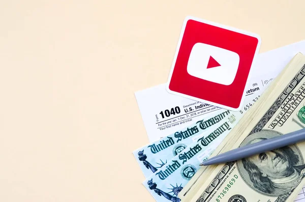 Youtube-gedrucktes Logo mit 1040 individuellen Einkommensteuererklärungen mit Rückerstattungsscheck und Hundert-Dollar-Scheinen auf beigem Hintergrund. Hilfe in Steuerzeit aus sozialem Netzwerk-Konzept — Stockfoto