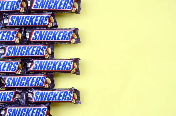 Veel Snickers chocoladerepen liggen op pastelgeel papier. Snickers bars worden geproduceerd door Mars Incorporated. Snickers is gemaakt door Franklin Clarence Mars in 1930. — Stockfoto