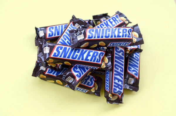 De nombreuses barres de chocolat Snickers reposent sur du papier jaune pastel. Les barres Snickers sont produites par Mars Incorporated. Snickers a été créé par Franklin Clarence Mars en 1930 — Photo