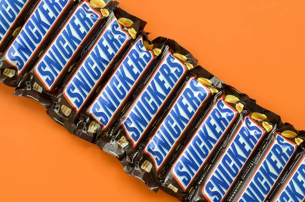 Veel Snickers chocoladerepen liggen op pasteloranje papier. Snickers bars worden geproduceerd door Mars Incorporated. Snickers is gemaakt door Franklin Clarence Mars in 1930. — Stockfoto