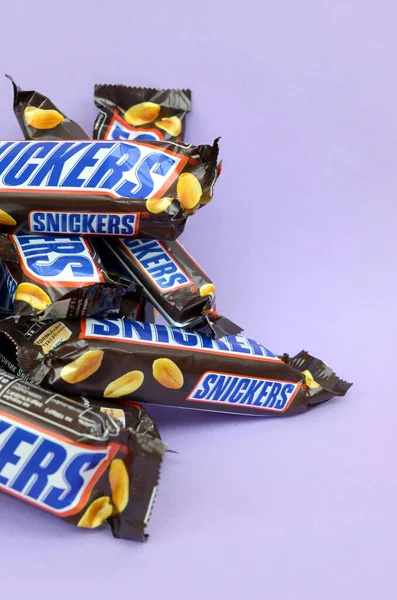 Veel Snickers chocoladerepen liggen op pastellila papier. Snickers bars worden geproduceerd door Mars Incorporated. Snickers is gemaakt door Franklin Clarence Mars in 1930. — Stockfoto